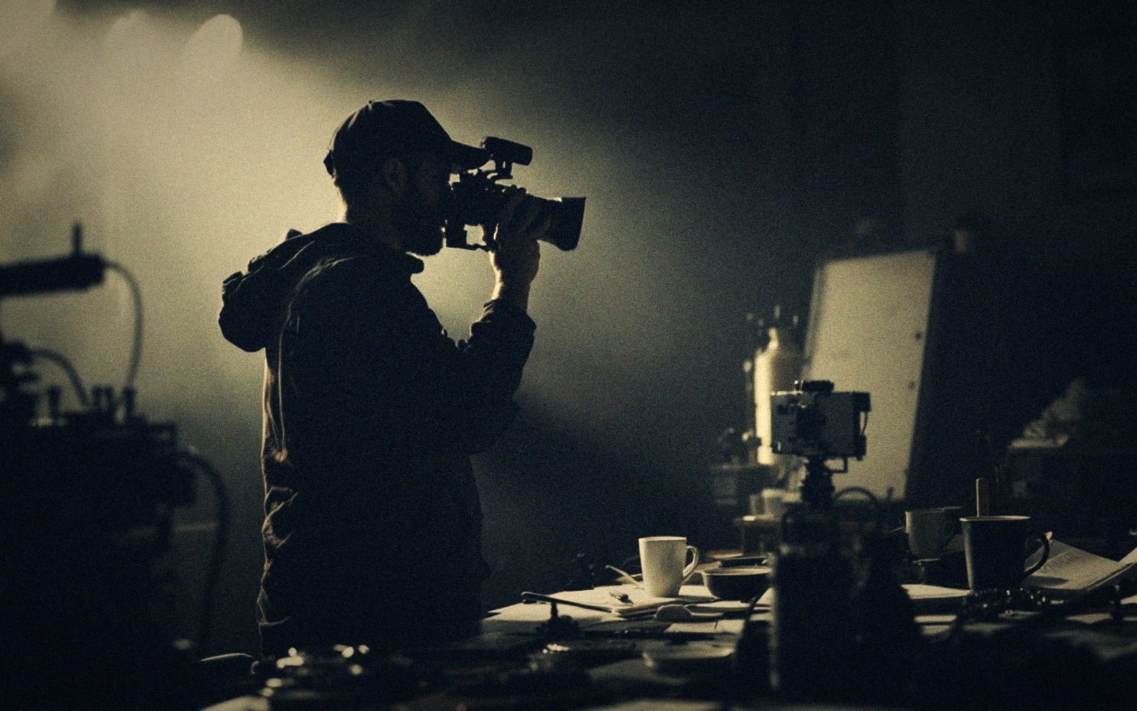 Silhouette of a filmmaker holding a camera to his eye on a dim set