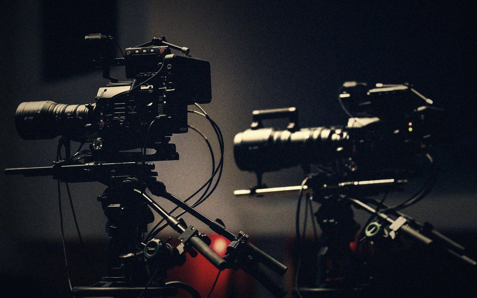 Two professional cinema cameras with long lenses mounted on tripods in a dim studio