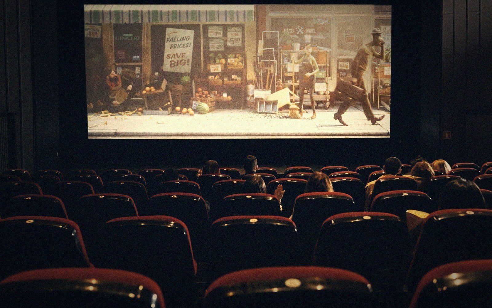 Audience watching a street-scene film in a movie theater with red seats