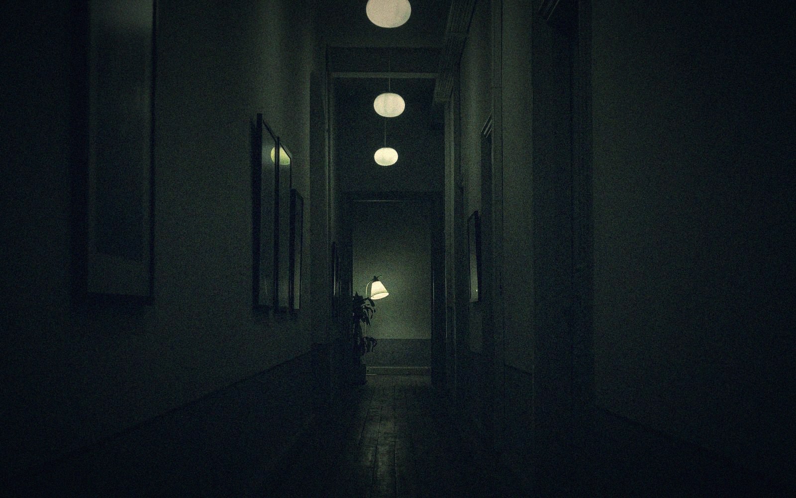 Dim hallway lit by hanging globe lamps leading toward a lamp-lit doorway