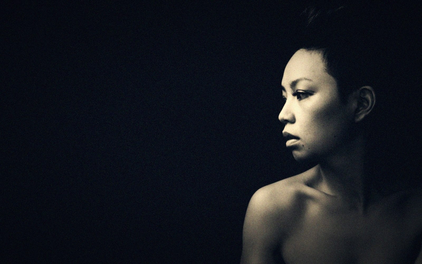 Woman in profile lit against a black background, bare shoulders visible