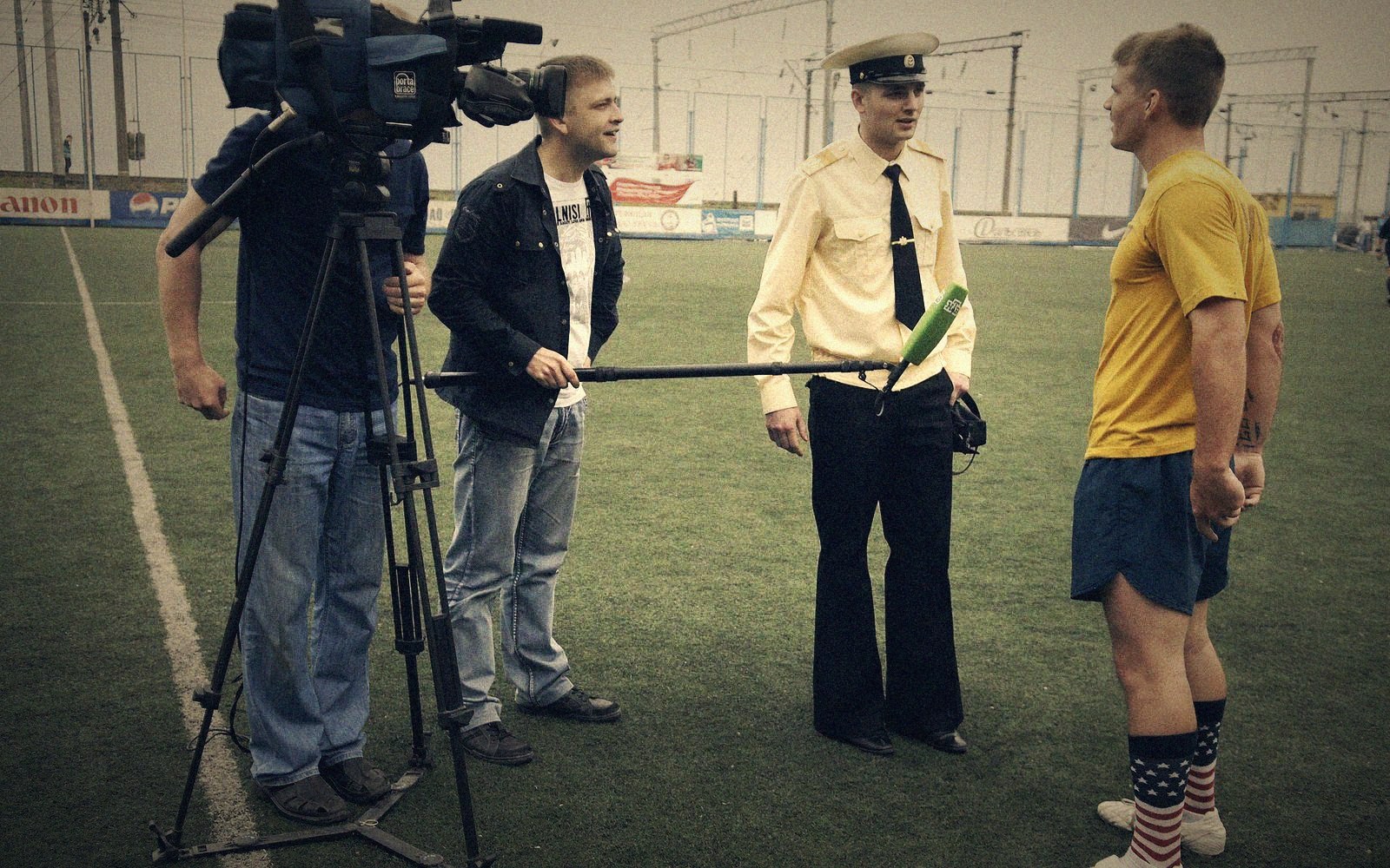 A camera crew films a uniformed officer and an athlete on a soccer field