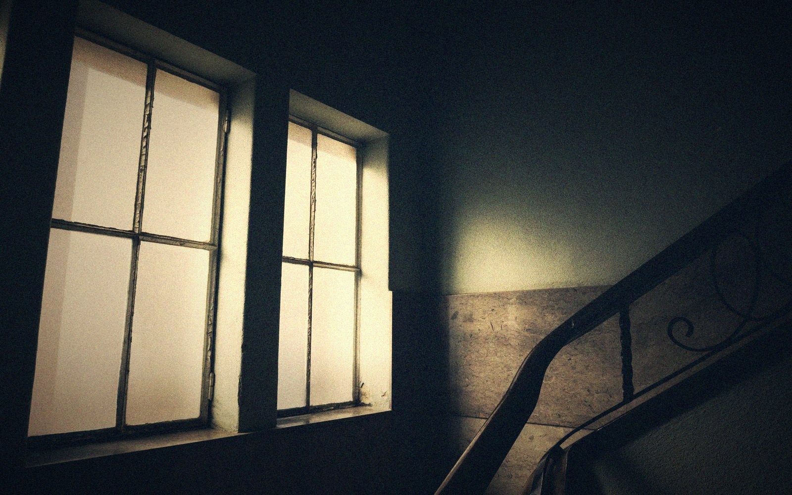 Sunlit windows beside a shadowy stairwell with an ornate wrought-iron railing