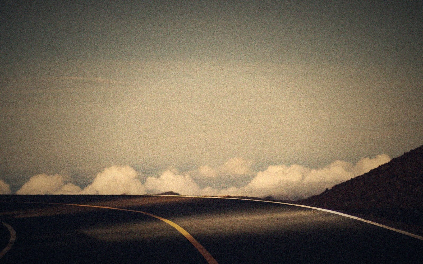 Curving mountain road disappearing into clouds below a dusky sky
