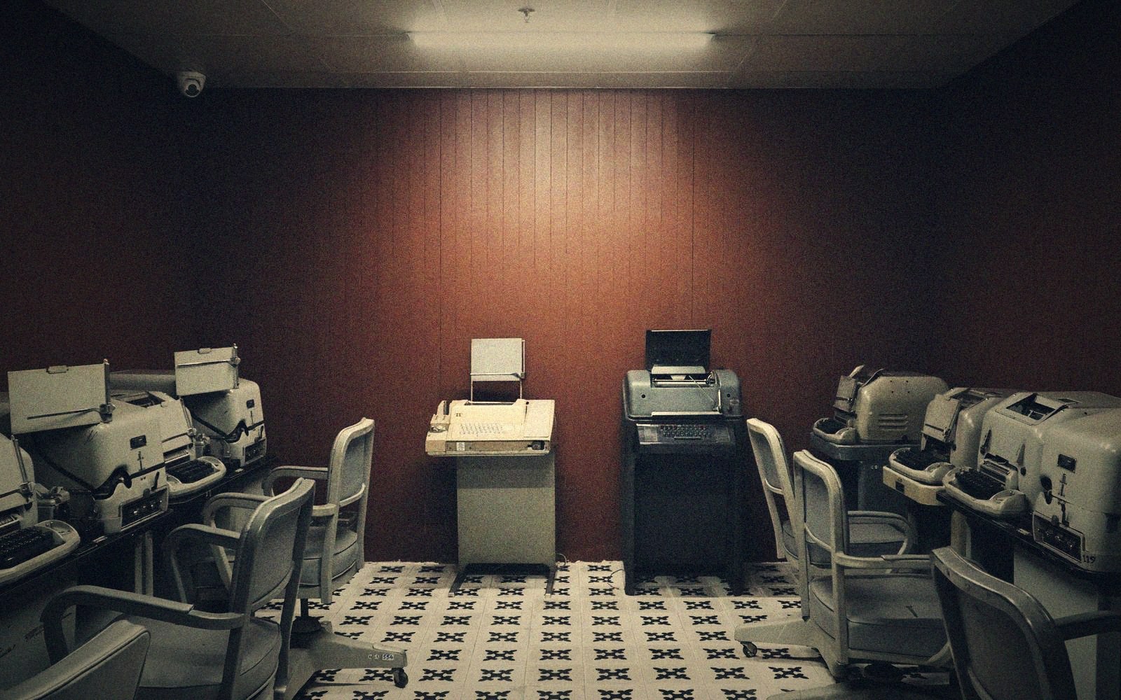 Rows of vintage teletype machines and chairs line a dimly lit wood-paneled room