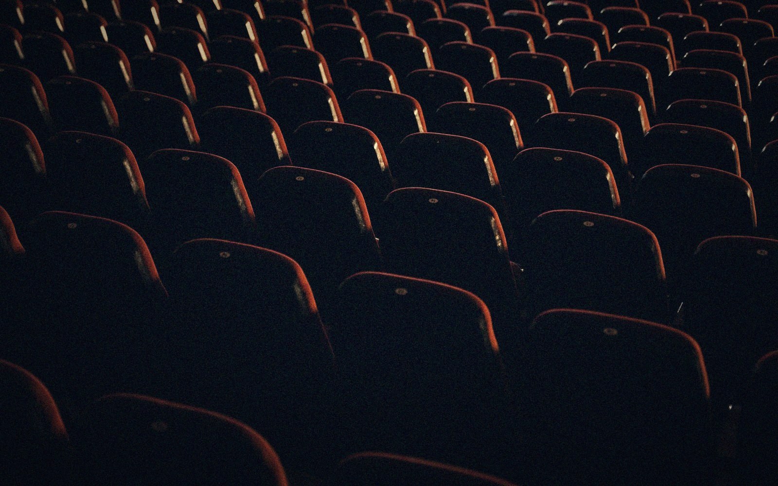 Rows of empty theater seats fade into darkness under dim red lighting