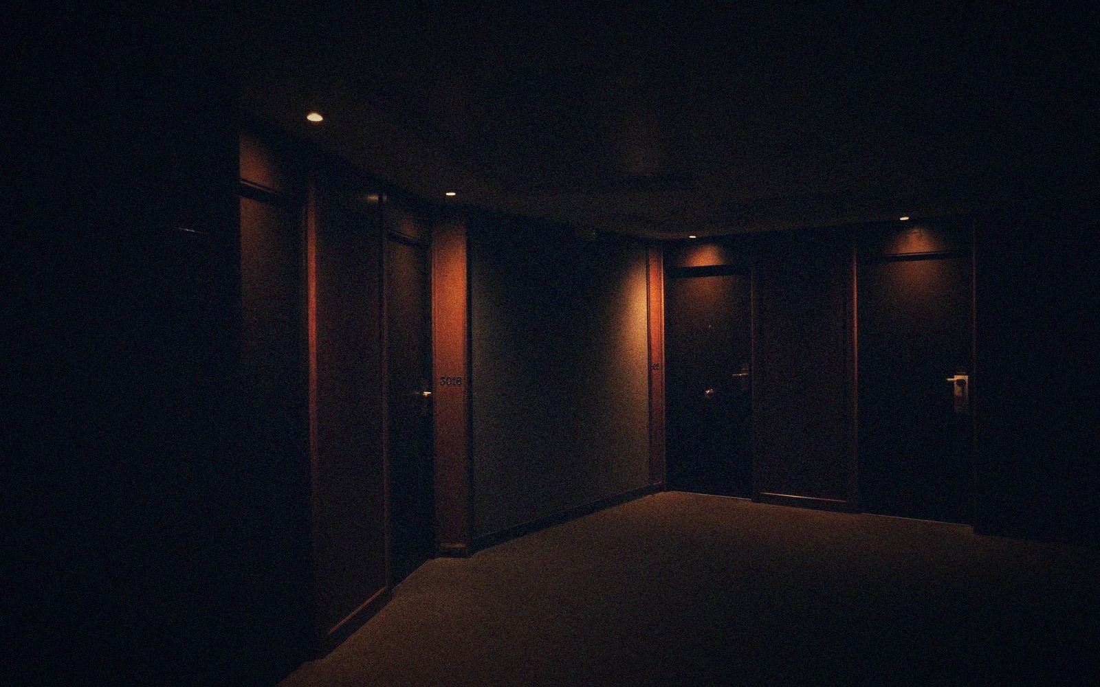Dimly lit hotel corridor with wooden doors and recessed ceiling spotlights